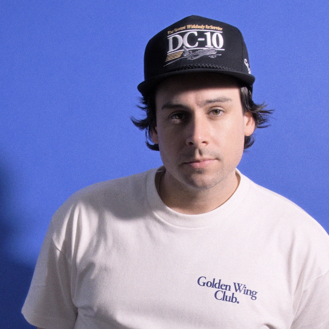 Man wearing DC-10 cap from Golden Wing club stands before blue baclground